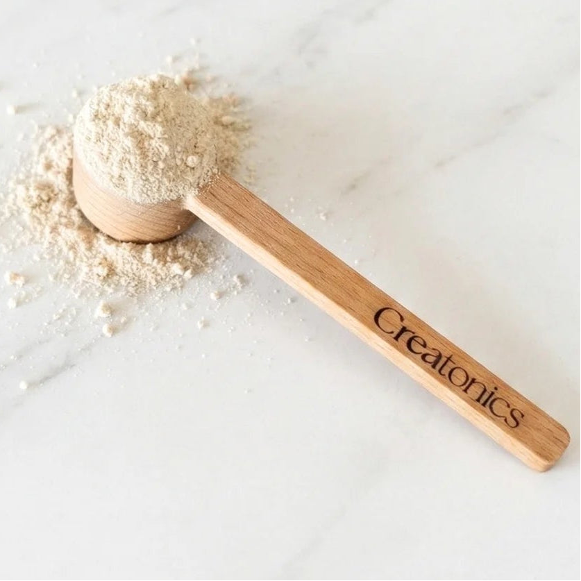 Wooden scoop with powder on a white surface, featuring the brand 'Creatonics'.