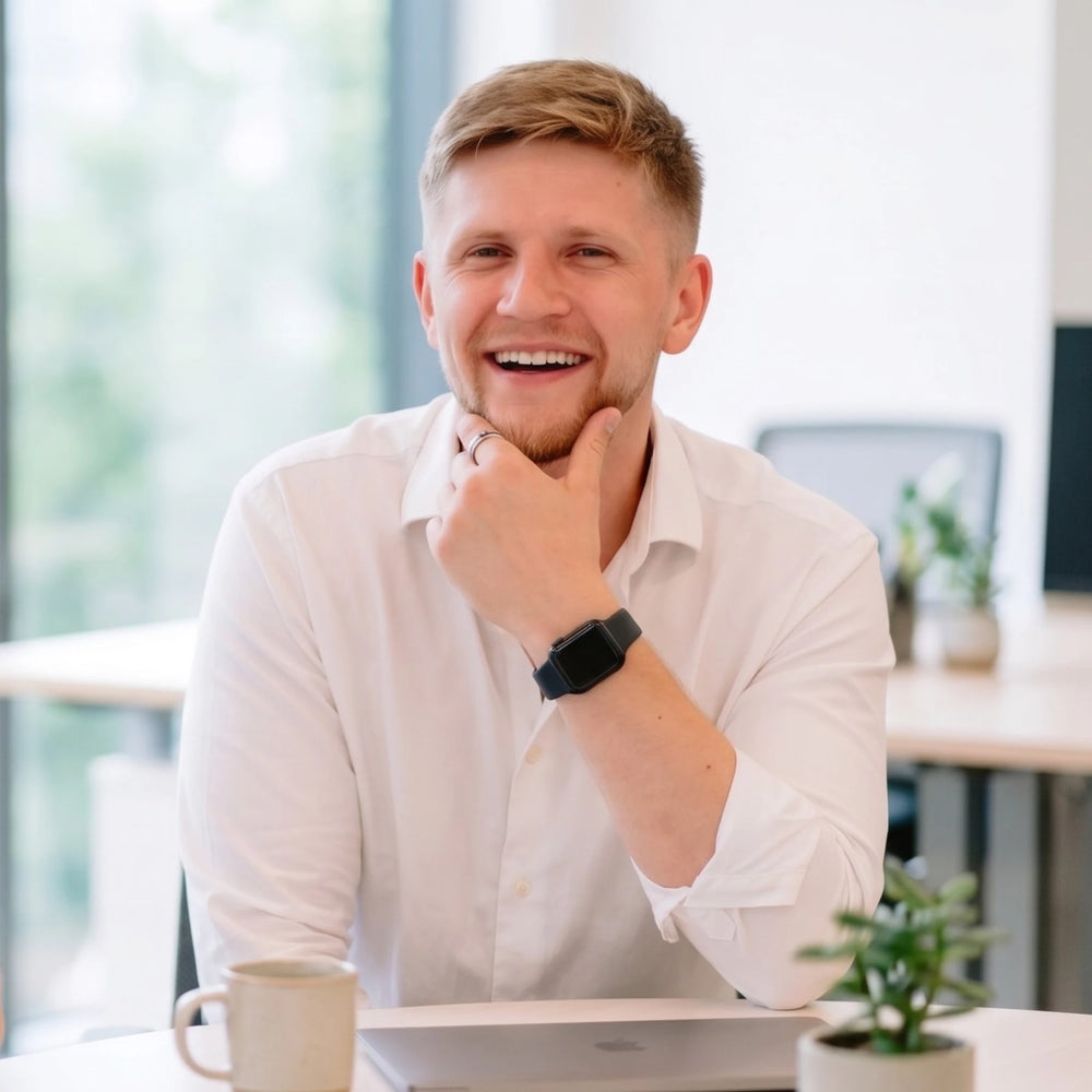 Creatonics co-founder, Chris Curwen, in a white shirt sitting at a desk with a laptop, smiling.