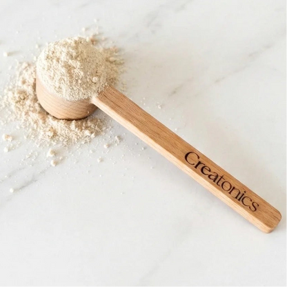 Wooden scoop with powder on a white surface, featuring the brand 'Creatonics'.
